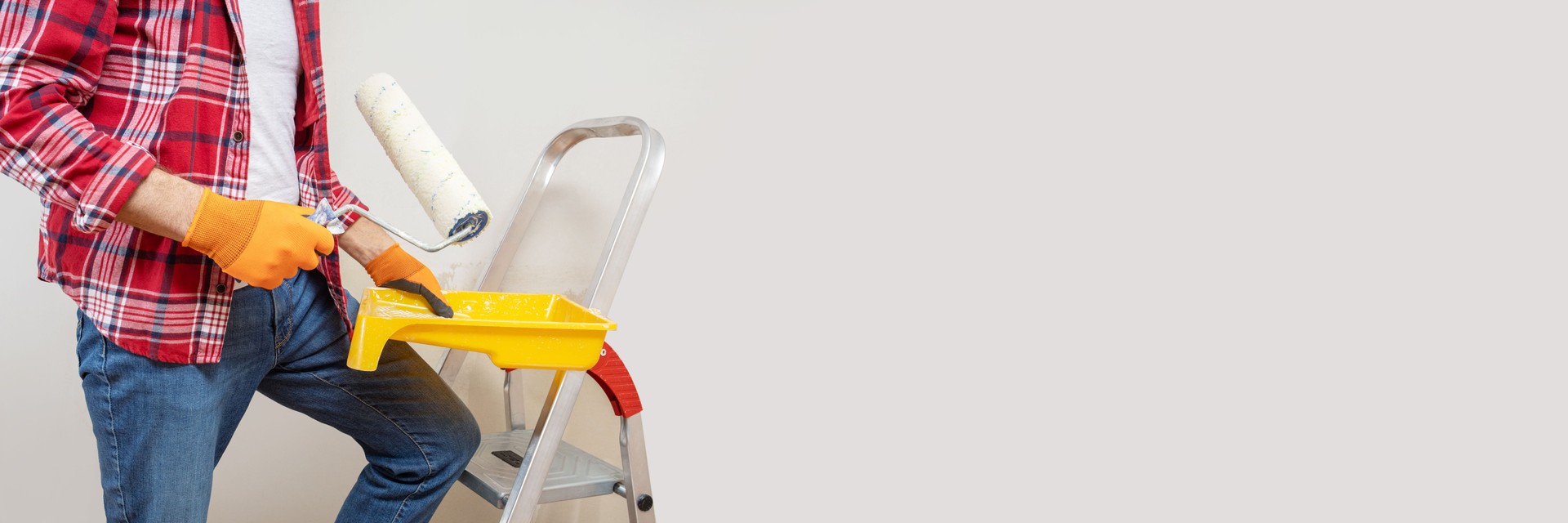 painter man at work with a paint roller, wall painting grey color. Long format. Panoramic banner with copy space.